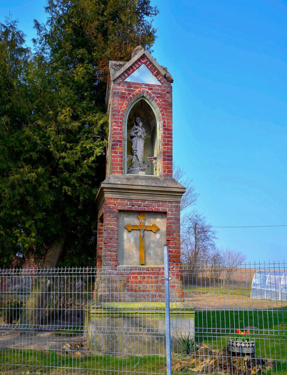 Kapliczka murowana wzniesiona w 1908 roku. We wnęce znajduje się figura Matki Boskiej z Dzieciątkiem. Szczęsne, gmina Purda, powiat olsztyński.